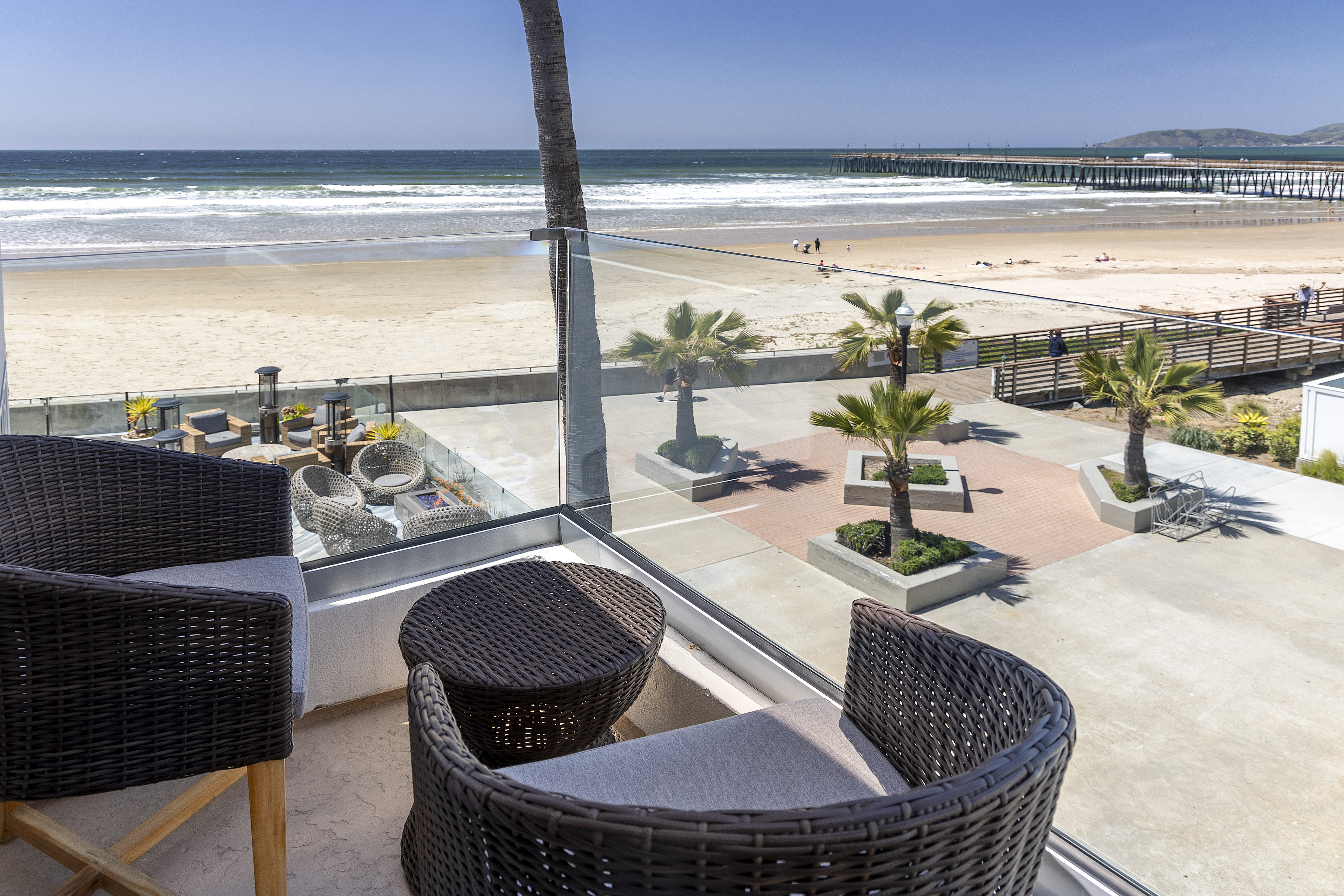 A beach view with a pier, palm trees, and outdoor furniture