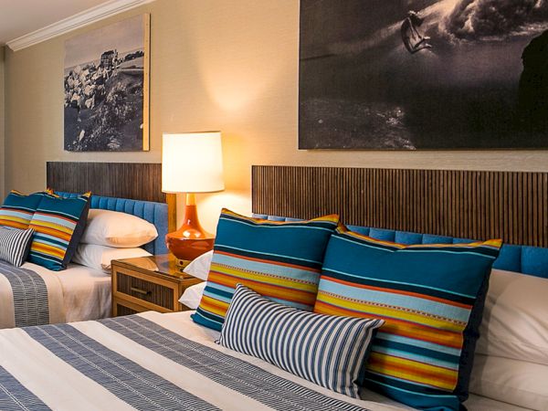 A hotel room with two double beds, blue striped pillows, a bedside lamp, framed ocean-themed art, and neutral tones.