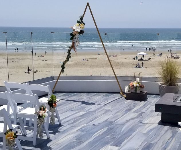 A wooden pier with a rope swing, a chair, and seagulls near the boards; ocean and beach visible in the background, sunny day.